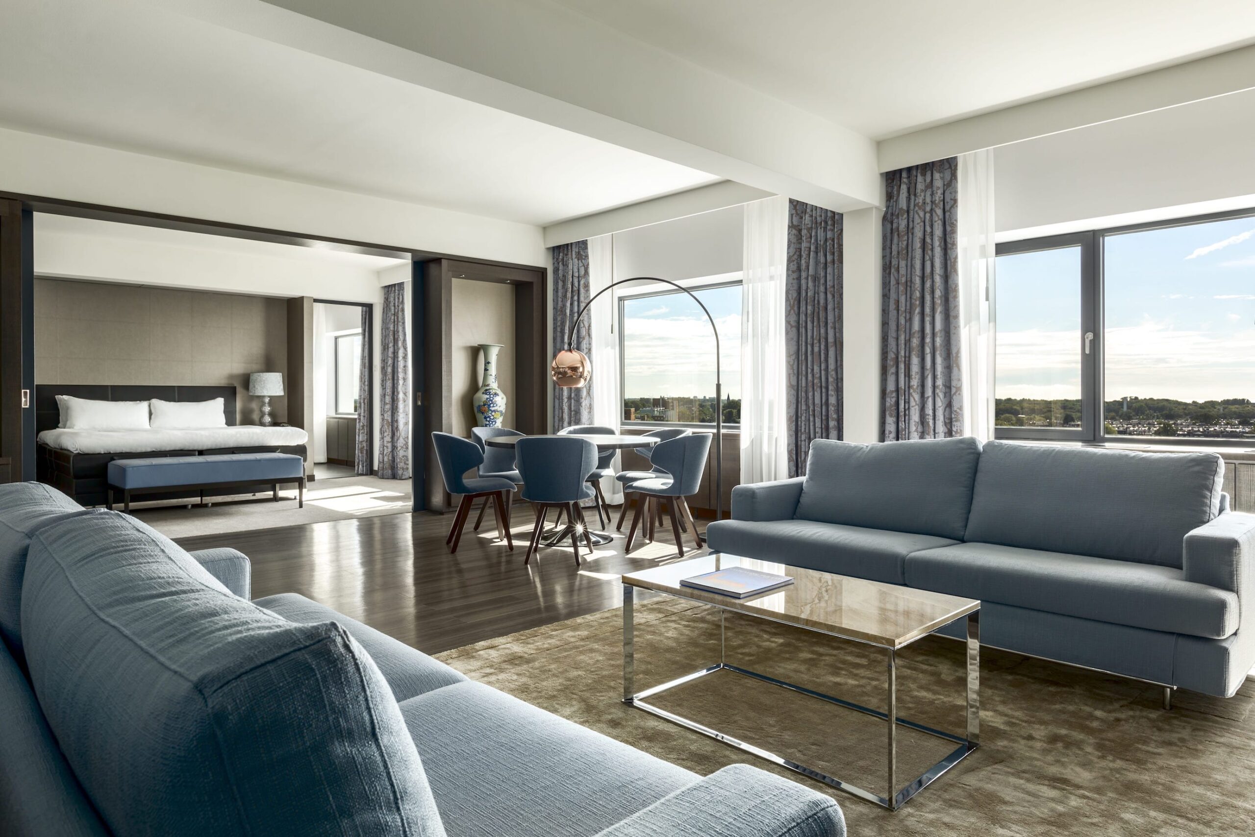 zona de estar de la habitación de hotel con sofás tapizados en tono gris, sillas y cortinas en tonos combinados
