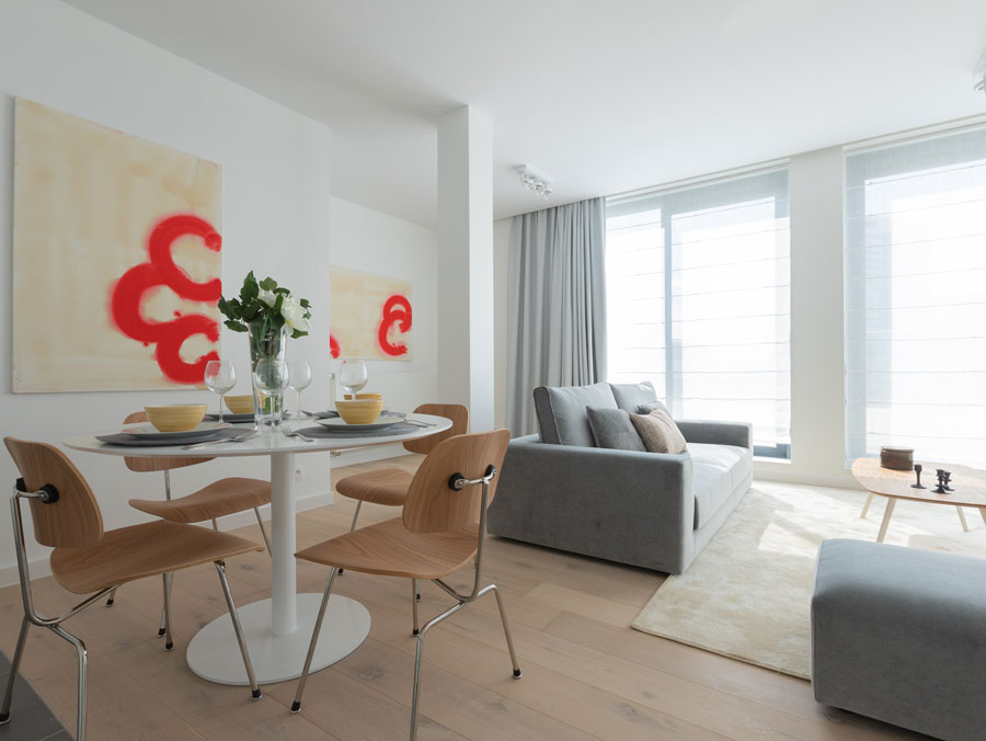 habitación de los apratamentos de Bruselas donde se ven cortinas y sofá tapizados en tonos neutros junto a una mesa de madera y sillas