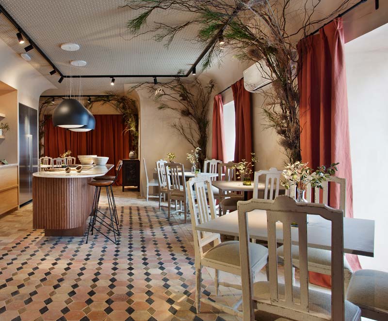 espacio de restaurante diseñado por Tristan Domec con alfombra geométrica, muebles en tono blanco, sillas tapizadas en tono gris y cortinas tono tierra