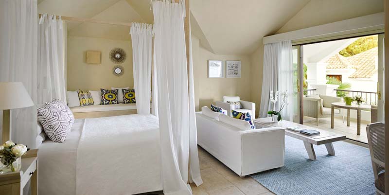 habitación con cama con dosel, cortinas, sofás en tono blanco y cojines de colores de gancedo