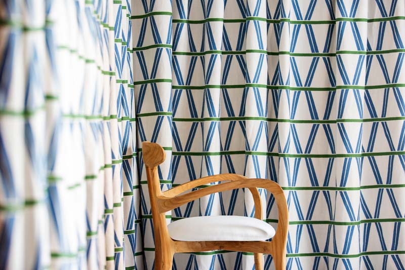 detalle de una esquina del córner compuesto por la cortina geométrica y una silla tapizada en tono beige