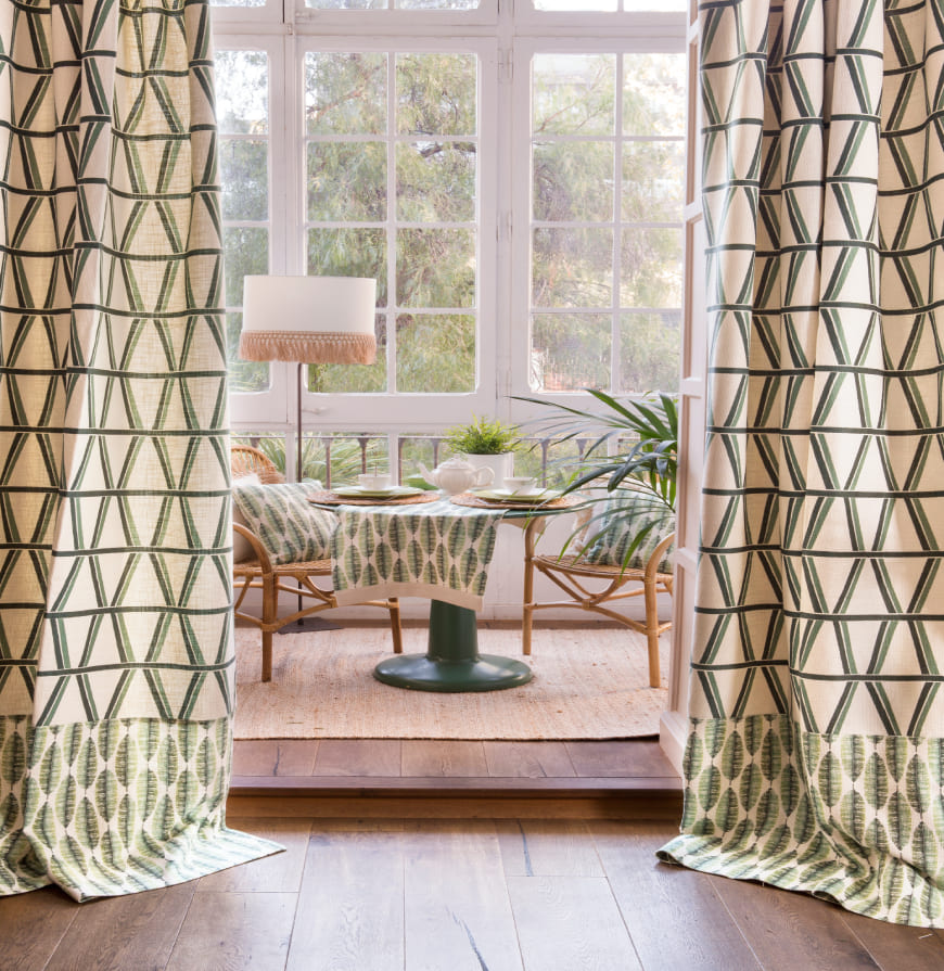 vista de habitación con cortinas geométricas en tonos verdes, mantel con diseño de hojas y cojines a juego