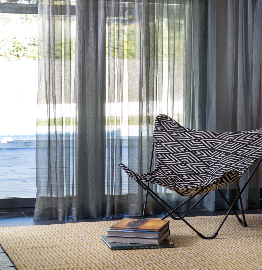 habitación con cortinas grises y sillón con tela geometrica negra y blanca, debajo alfombra geométrica en tonos amarillo y beige