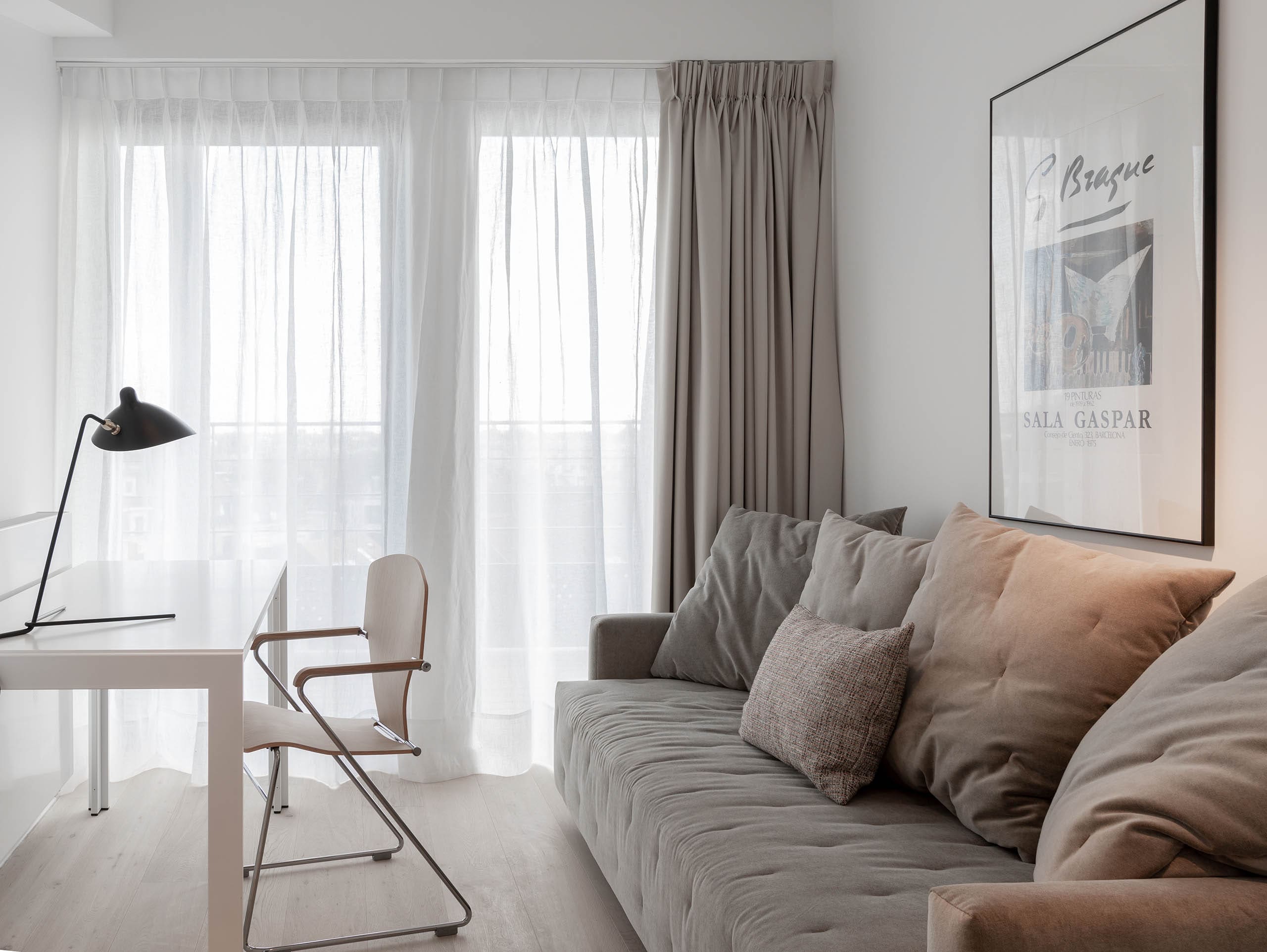 zona de estar de la habitación con un sofá tapizado en tono beige, visillos y opacantes en tono neutro