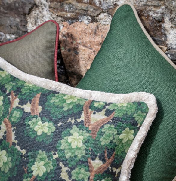 detalle cojines verdes, alfondo dos lisos verdes y en primer plano uno con tejido de verduras verdes y espumillón en el contorno.