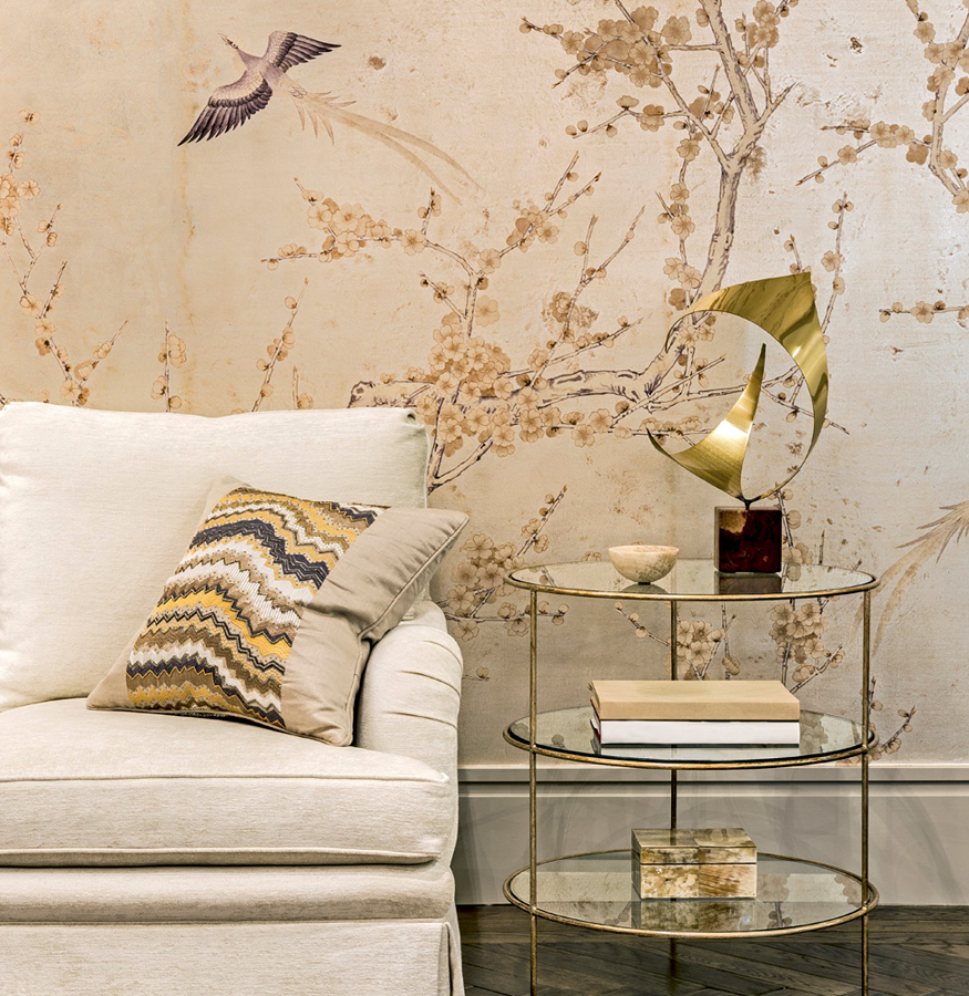 salón con papel pintado de motivos vegetales tierra y griss con forma de árbol, con un sofá tapizado en tono beige, cojín y mesa de café