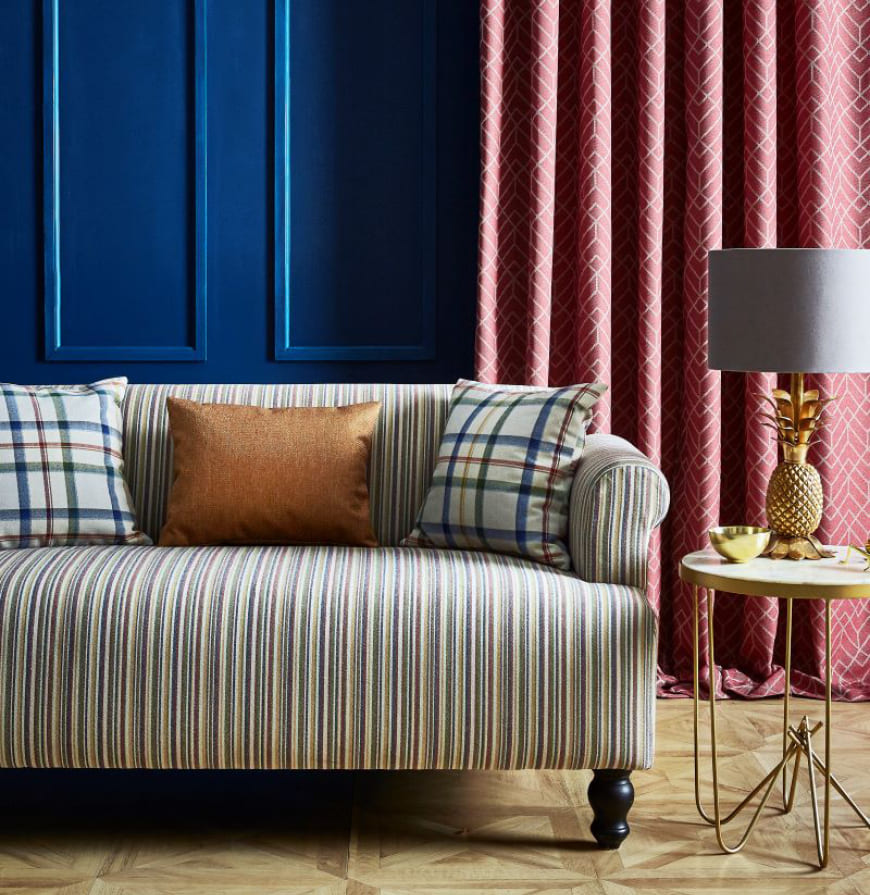 salón con sofá de rayas de colores, cojines de cuadros tartán y cortinas geométricas en tonos rosas