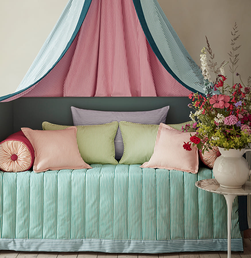 cama con colcha, dosel y cojines de rayas en combinación de colores verdes, anaranjados y rosas