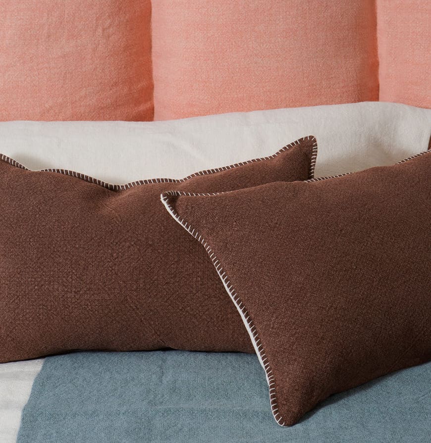 cabecero de cama en tono rosas, almohadón blanco y cojines tierra con detalle en la costura sobre colcha azul