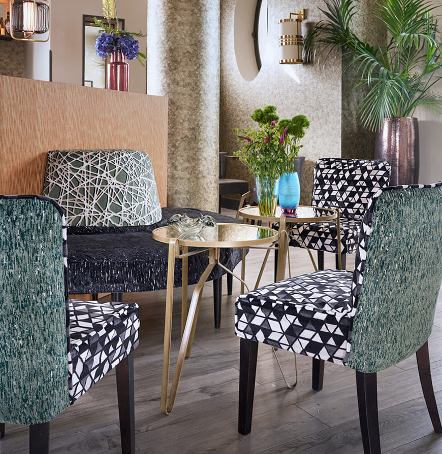 zona común de bar de hotel con un banco y sillas tapizadas con tejidos geométricos en tonos azul y verde