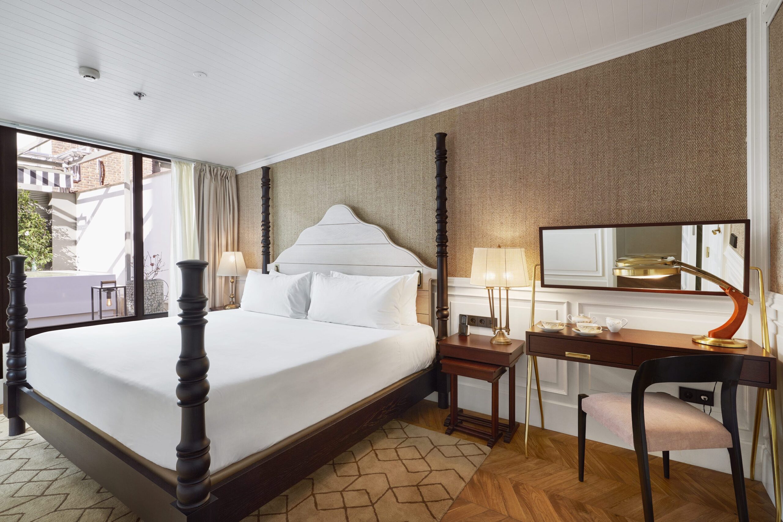 habitación de hotel con alfombra geométrica personalizada, parededes enteladas y cortinas en tonos naturales