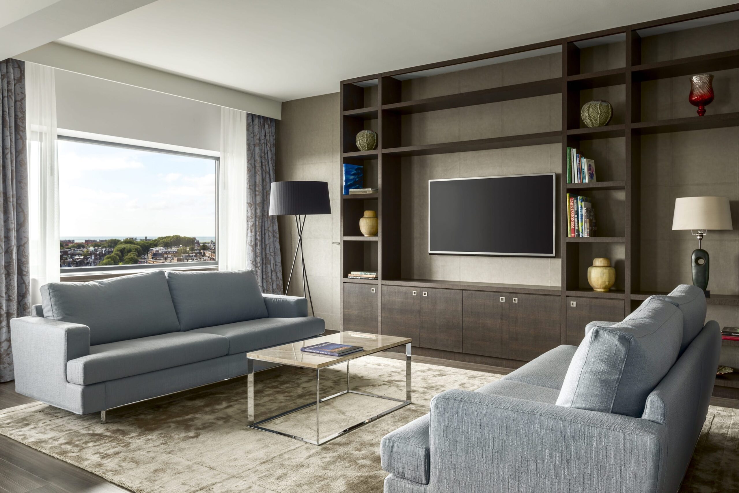 sala de estar de hotel con sofás tapizados con textil gris, blackouts y visillos en tono neutro